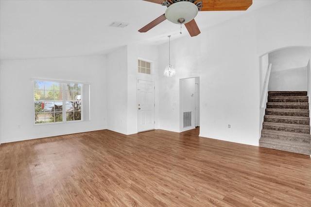 unfurnished living room featuring ceiling fan with notable chandelier, high vaulted ceiling, and wood-type flooring