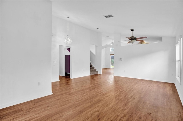 unfurnished living room with ceiling fan with notable chandelier, a towering ceiling, and wood-type flooring