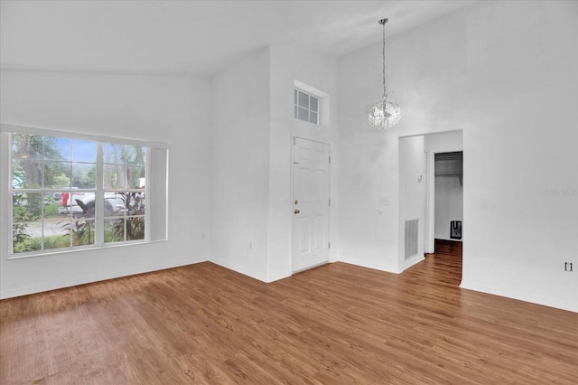 unfurnished room with a wealth of natural light, high vaulted ceiling, a notable chandelier, and wood-type flooring