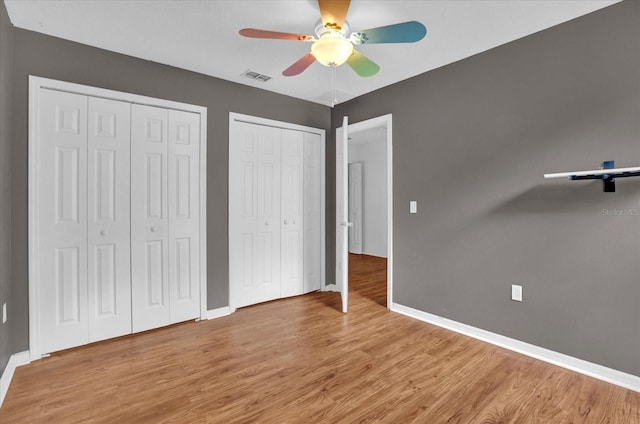 unfurnished bedroom featuring hardwood / wood-style flooring, two closets, and ceiling fan