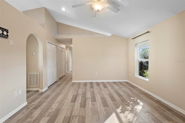 empty room featuring arched walkways, visible vents, vaulted ceiling, and light wood-style flooring