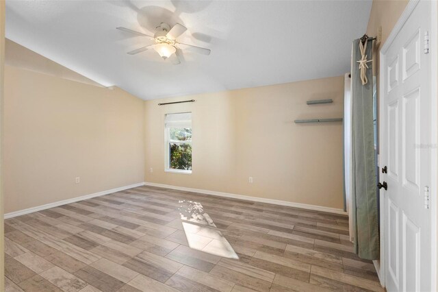 empty room with light wood-type flooring, baseboards, vaulted ceiling, and a ceiling fan