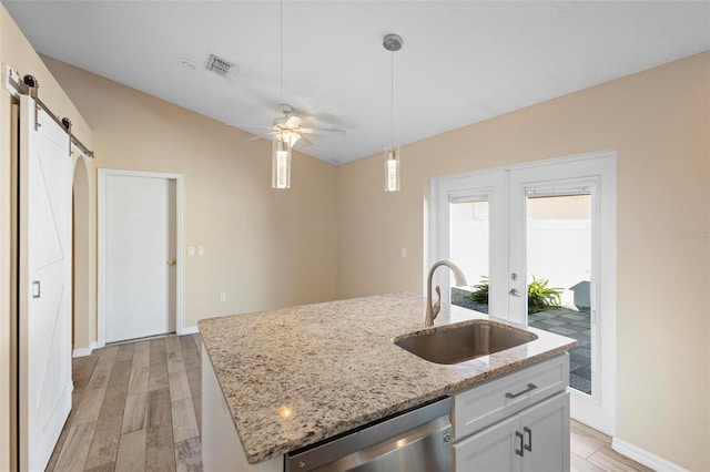 kitchen featuring a barn door, visible vents, dishwasher, decorative light fixtures, and a sink