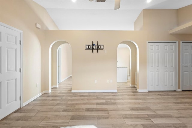 empty room with arched walkways, a ceiling fan, wood tiled floor, high vaulted ceiling, and baseboards