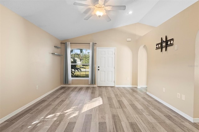 unfurnished room with arched walkways, a ceiling fan, baseboards, vaulted ceiling, and light wood finished floors