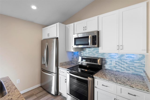 kitchen featuring light stone countertops, vaulted ceiling, stainless steel appliances, white cabinetry, and backsplash