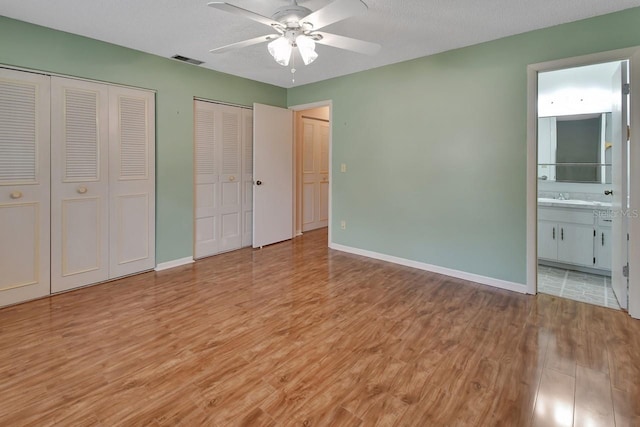 unfurnished bedroom featuring ceiling fan, ensuite bathroom, light hardwood / wood-style flooring, and multiple closets