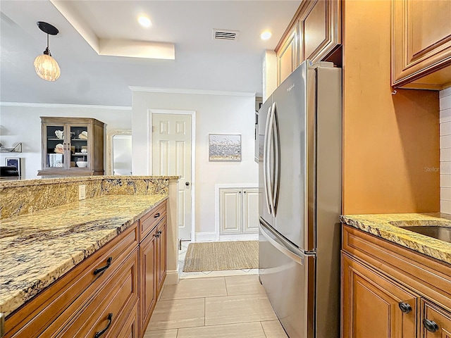 kitchen with light tile patterned floors, light stone countertops, stainless steel refrigerator, pendant lighting, and ornamental molding