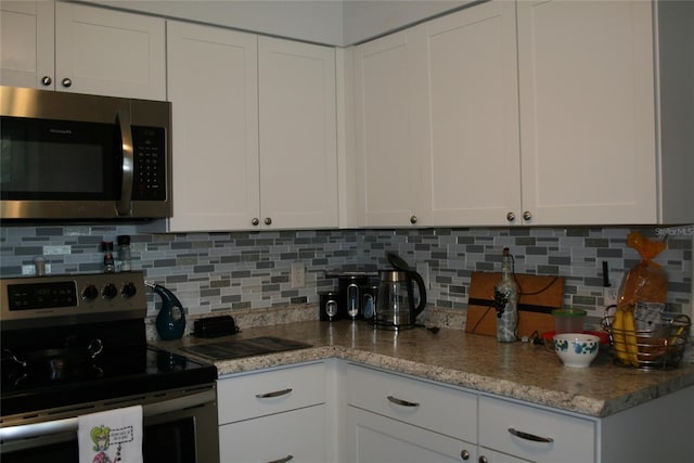 kitchen with light stone countertops, white cabinetry, appliances with stainless steel finishes, and backsplash