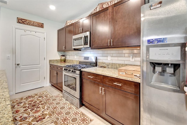 kitchen with light tile patterned floors, light stone counters, dark brown cabinetry, appliances with stainless steel finishes, and decorative backsplash