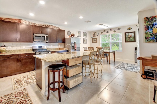 kitchen with light tile patterned floors, stainless steel appliances, visible vents, backsplash, and a kitchen bar