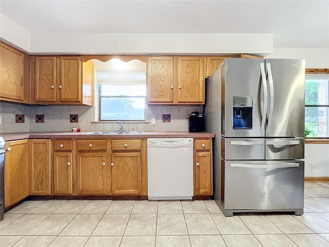 kitchen with tasteful backsplash, white dishwasher, light tile patterned floors, sink, and stainless steel fridge