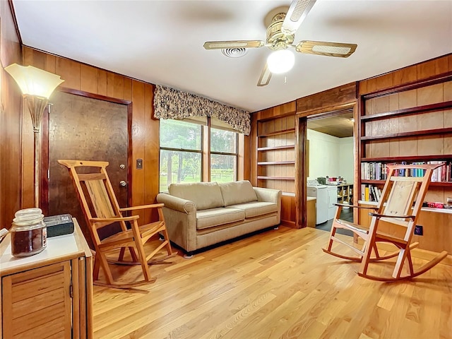 living area featuring light wood-type flooring, washer / dryer, ceiling fan, and wooden walls