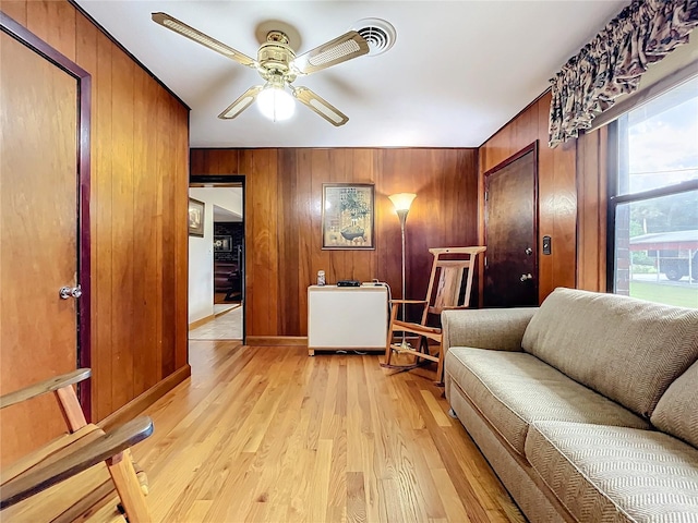 living room with ceiling fan, light wood-type flooring, and wood walls