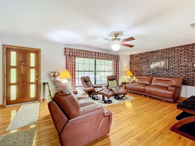 living area featuring brick wall, ceiling fan, wood finished floors, and visible vents