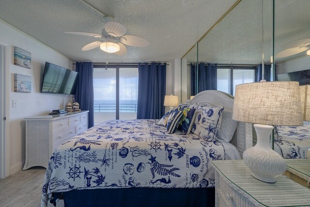 bedroom with a textured ceiling, ceiling fan, expansive windows, and light hardwood / wood-style floors