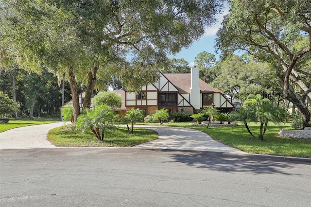 english style home featuring driveway, a chimney, and a front lawn