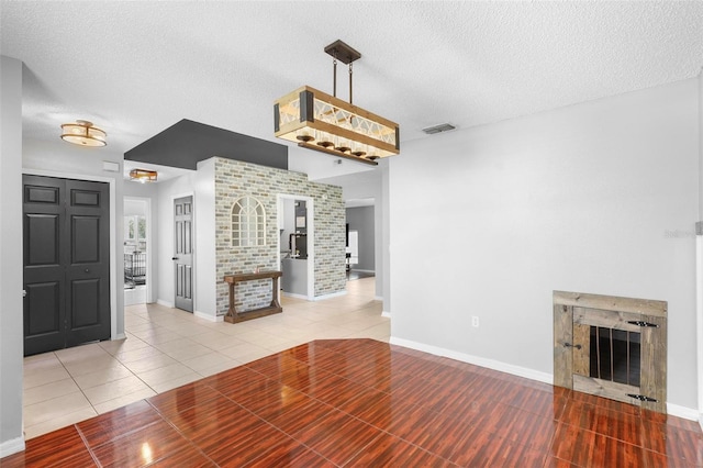 unfurnished living room featuring a textured ceiling, brick wall, light tile patterned floors, and a fireplace