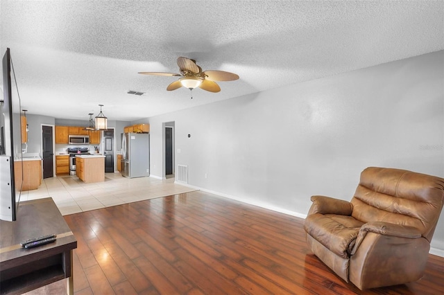 living room with a textured ceiling, light hardwood / wood-style flooring, and ceiling fan