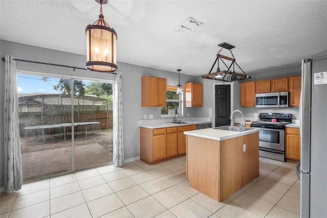 kitchen with pendant lighting, light tile patterned floors, a kitchen island with sink, stainless steel appliances, and sink