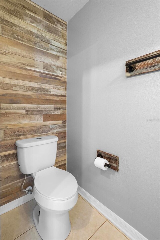 bathroom with wood walls, toilet, and tile patterned floors