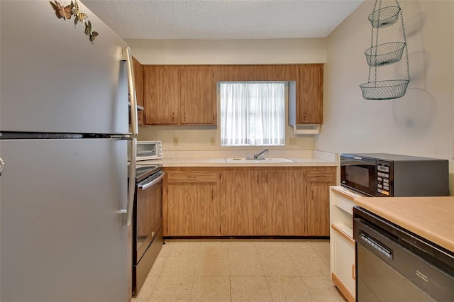 kitchen with freestanding refrigerator, stainless steel electric stove, light floors, black microwave, and a sink