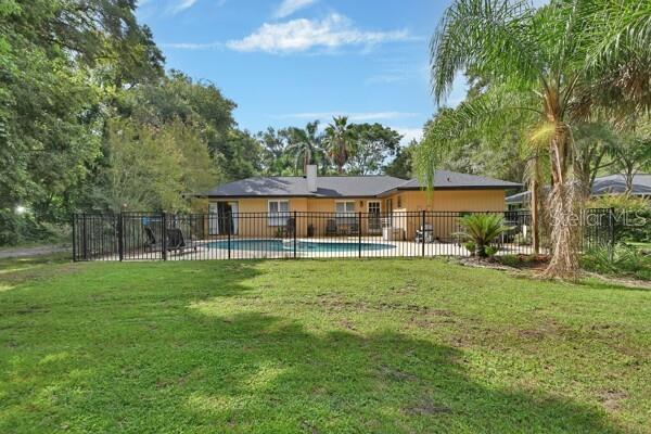 back of house featuring a fenced in pool and a lawn