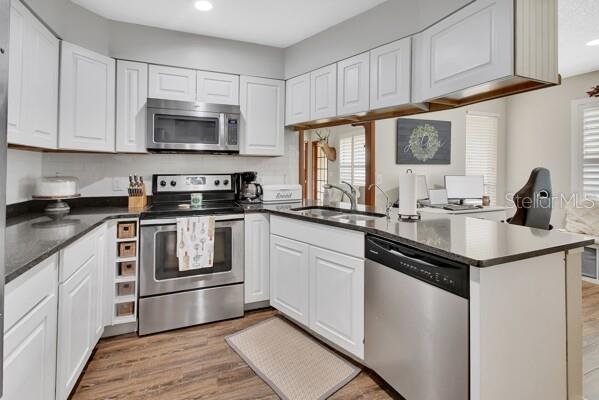 kitchen featuring kitchen peninsula, sink, appliances with stainless steel finishes, white cabinets, and light hardwood / wood-style floors