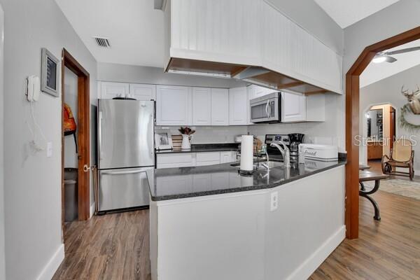 kitchen featuring stainless steel appliances, white cabinetry, dark hardwood / wood-style floors, kitchen peninsula, and ceiling fan