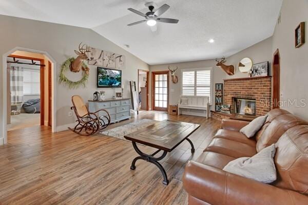 living room with ceiling fan, wood-type flooring, vaulted ceiling, and a brick fireplace