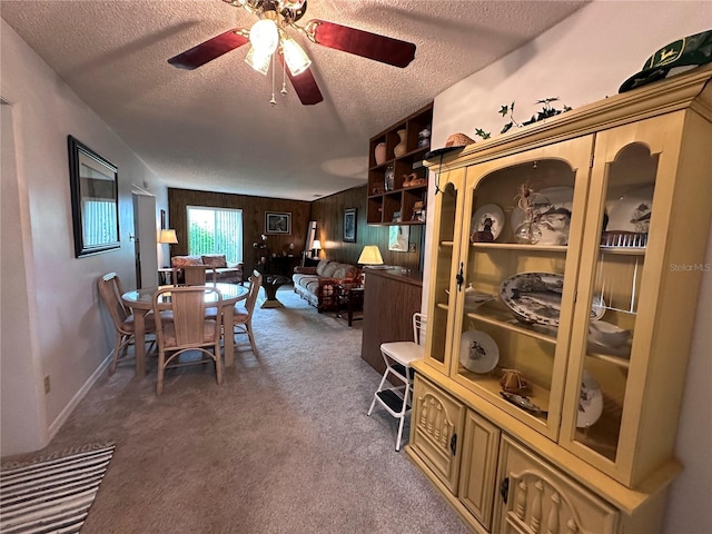 dining area featuring a textured ceiling, wood walls, dark colored carpet, and ceiling fan