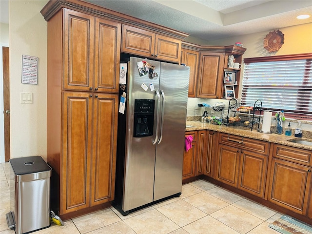 kitchen featuring a textured ceiling, light tile patterned flooring, stainless steel fridge, and light stone countertops