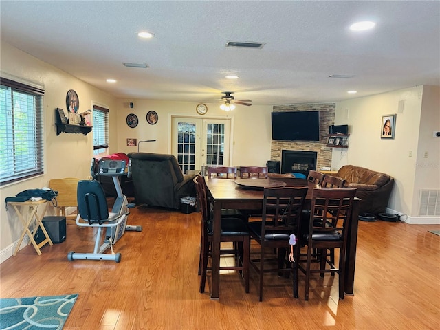 dining area featuring a textured ceiling, a stone fireplace, french doors, hardwood / wood-style flooring, and ceiling fan