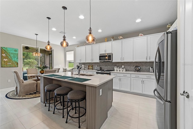 kitchen featuring appliances with stainless steel finishes, a kitchen island with sink, hanging light fixtures, sink, and white cabinetry