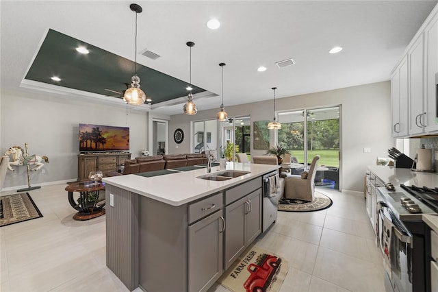 kitchen with white cabinets, appliances with stainless steel finishes, sink, pendant lighting, and a kitchen island with sink