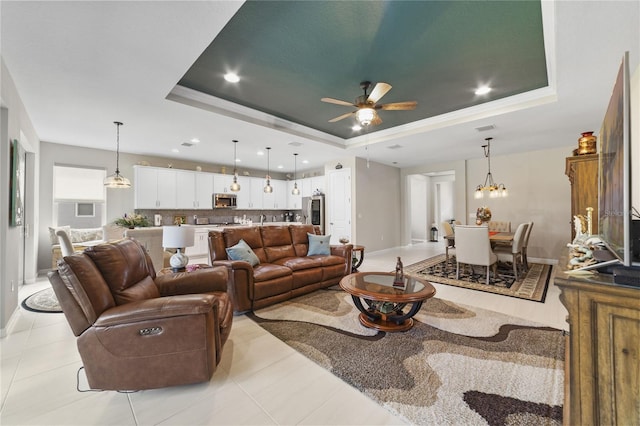 living room with ceiling fan with notable chandelier, light tile patterned floors, and a raised ceiling