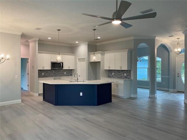 kitchen with white cabinets, pendant lighting, an island with sink, and light hardwood / wood-style floors