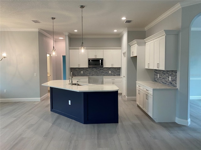 kitchen with a kitchen island with sink, light wood-type flooring, crown molding, backsplash, and white cabinets