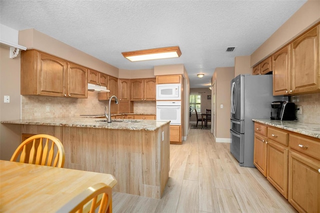 kitchen with a textured ceiling, light stone counters, light wood-type flooring, and white appliances