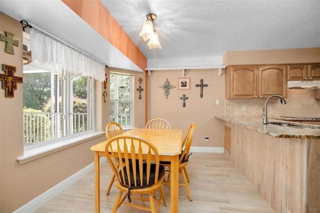 dining space featuring light wood-type flooring, sink, and a textured ceiling