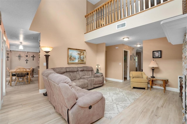 living room with a high ceiling, a textured ceiling, and light hardwood / wood-style flooring