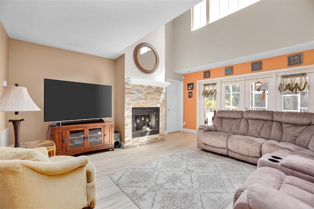 living room with high vaulted ceiling, a stone fireplace, and light wood-type flooring