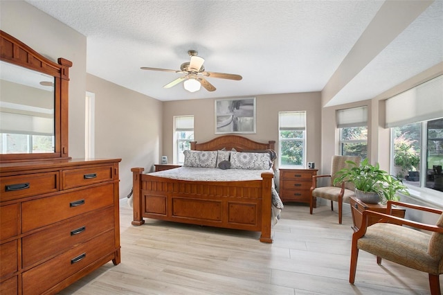 bedroom with a textured ceiling, ceiling fan, multiple windows, and light hardwood / wood-style floors