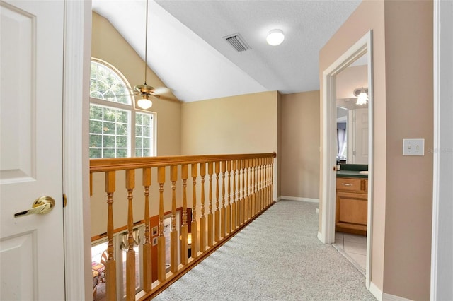 hallway featuring lofted ceiling, light colored carpet, and a textured ceiling