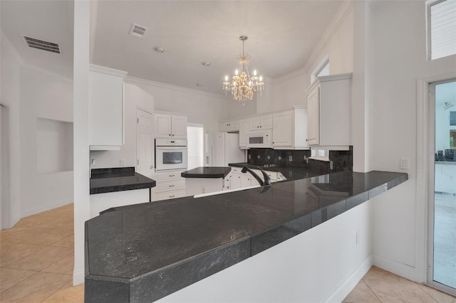 kitchen featuring kitchen peninsula, an inviting chandelier, white appliances, and white cabinetry