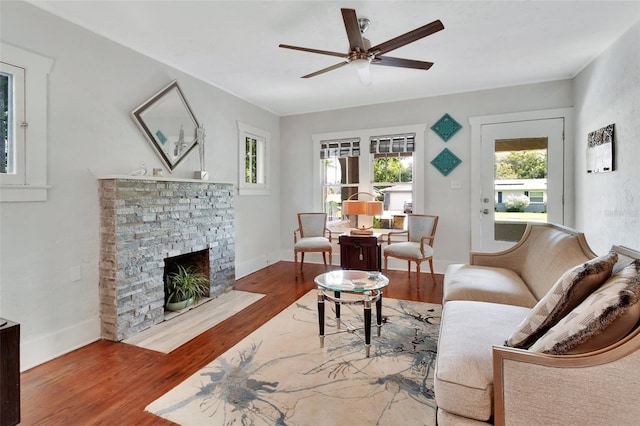 living room with ceiling fan, hardwood / wood-style floors, and a stone fireplace