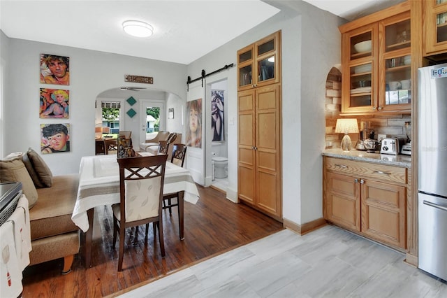 kitchen with a barn door, stainless steel fridge, light stone countertops, and light wood-type flooring