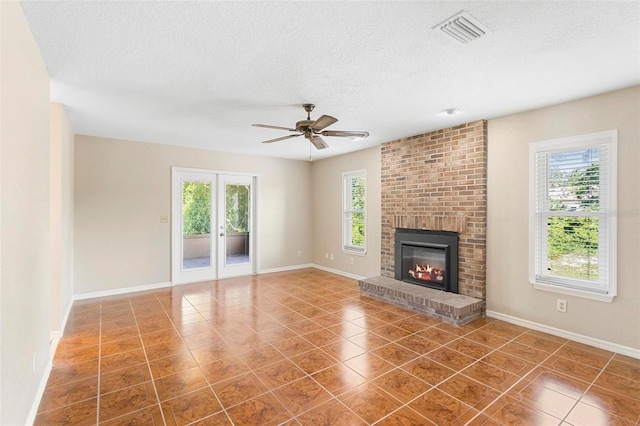 unfurnished living room featuring a fireplace, a textured ceiling, a wealth of natural light, and ceiling fan