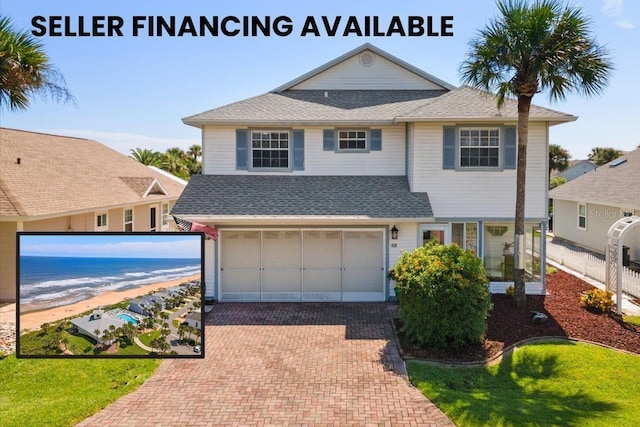 traditional-style house with a garage, a shingled roof, a beach view, a water view, and decorative driveway