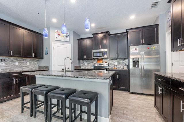 kitchen featuring a textured ceiling, sink, stainless steel appliances, a center island with sink, and dark brown cabinetry